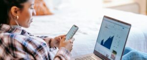 A woman checks her financial growth on a smartphone with a laptop open to analytics, representing smart affiliate marketing management.